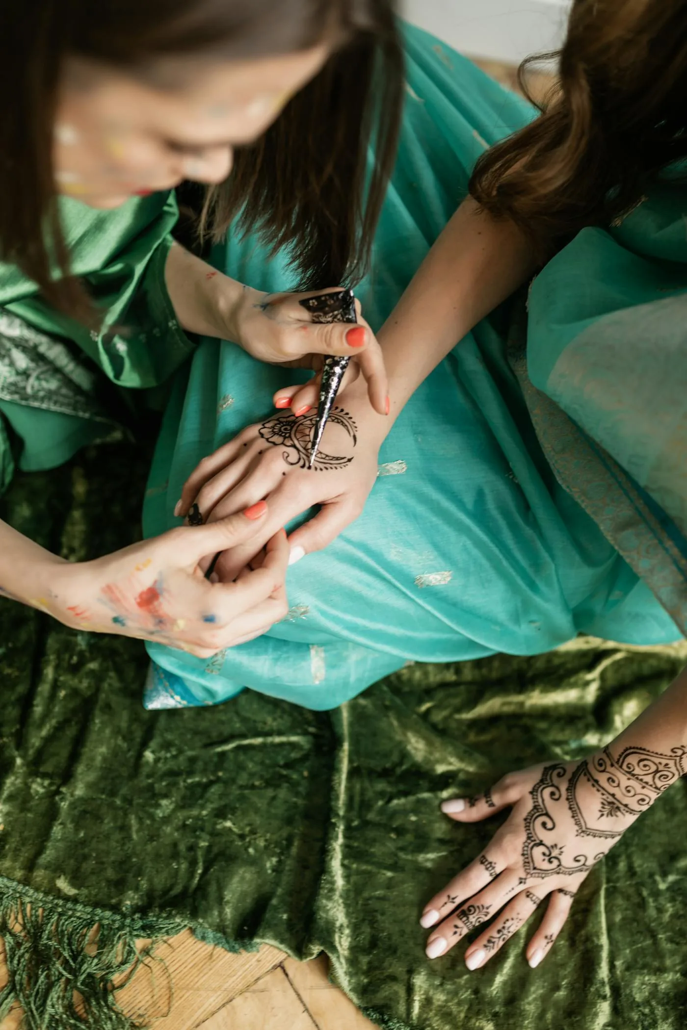 Henna cone applying a floral design to the back of a hand, artist and client seated together